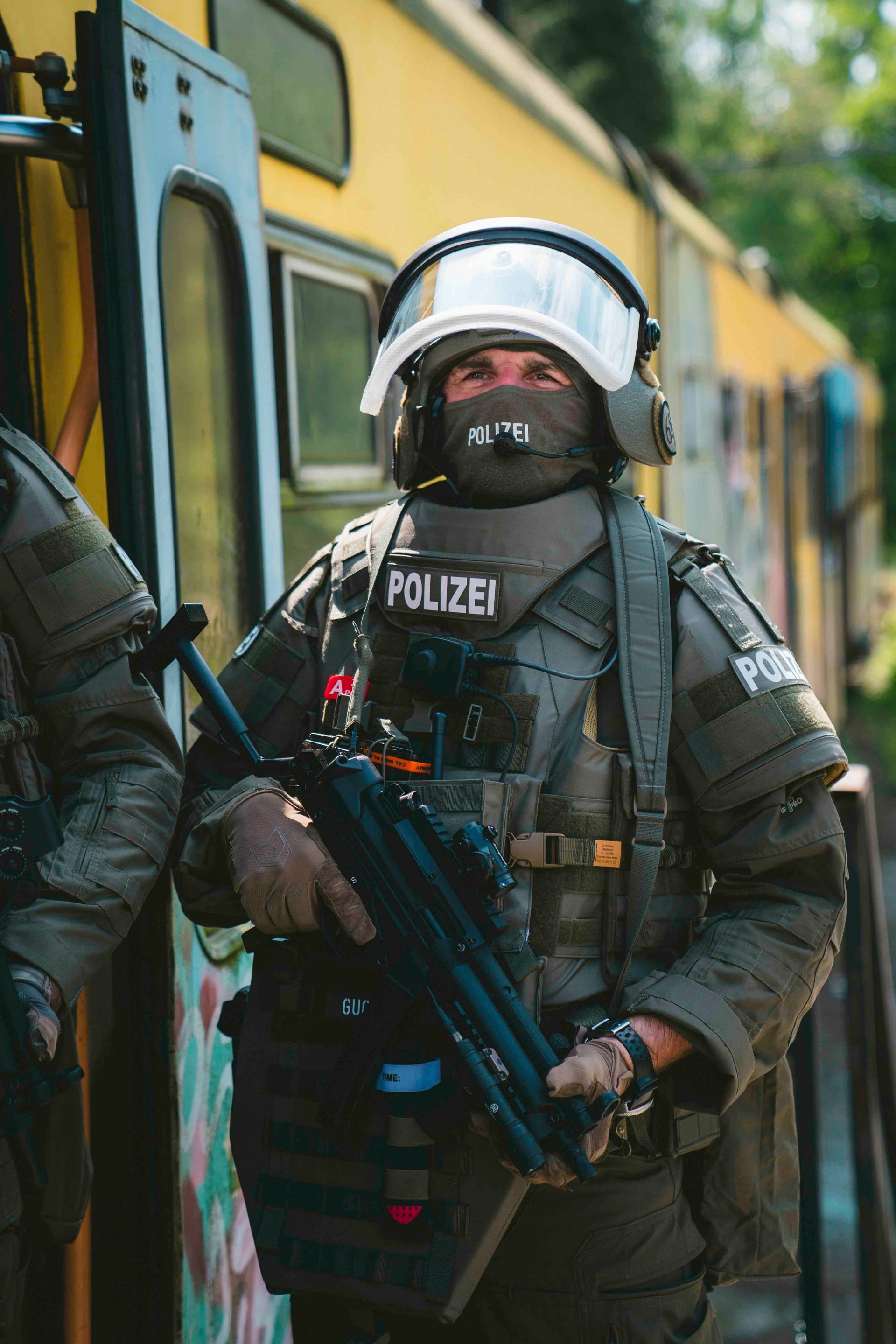 Ein Polizist in taktischer Ausrüstung, der eine Waffe hält, steht in der Nähe eines gelben Zuges.