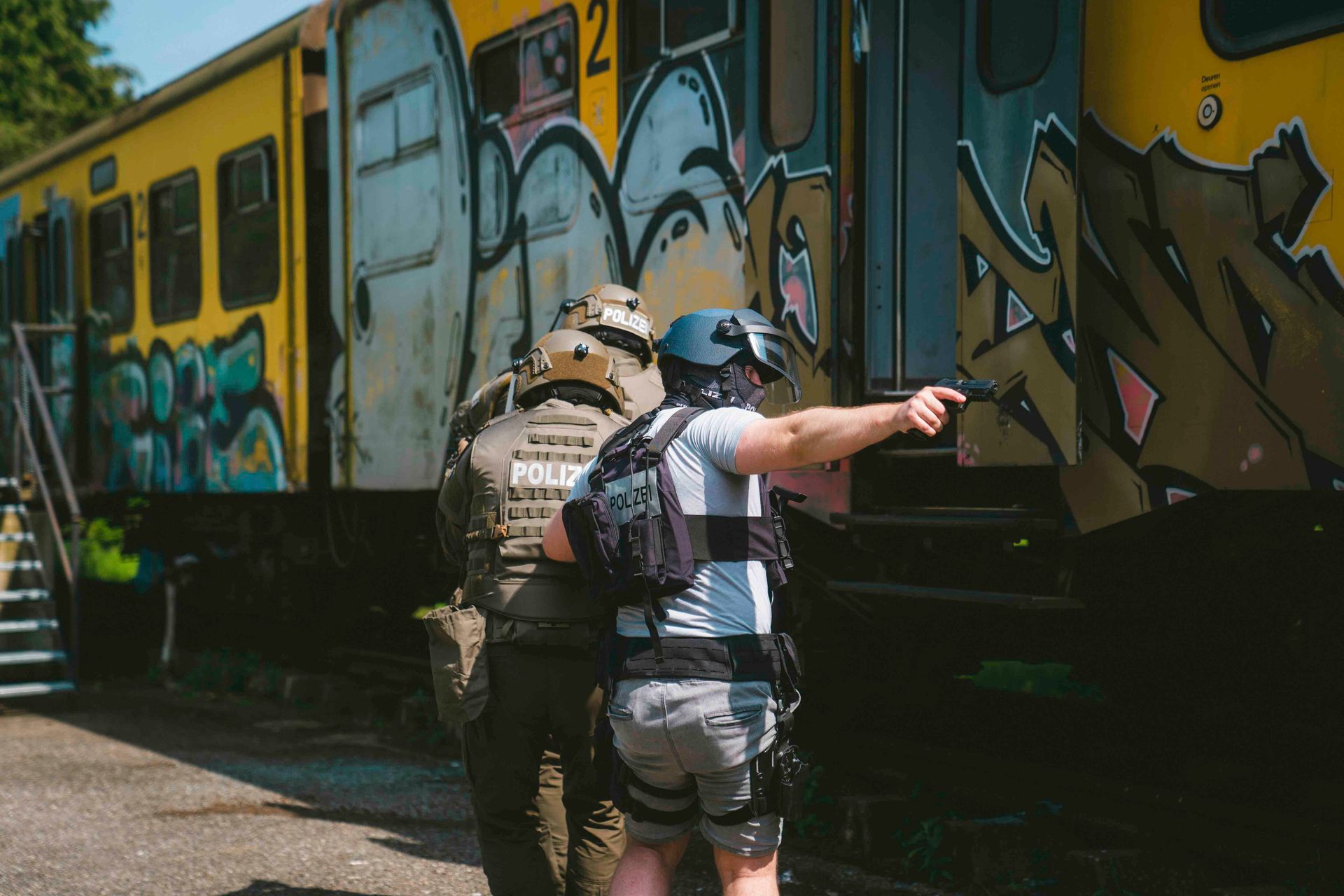 Zwei Polizisten mit gezogenen Waffen zielen in der Nähe eines mit Graffiti besprühten Eisenbahnwaggons.