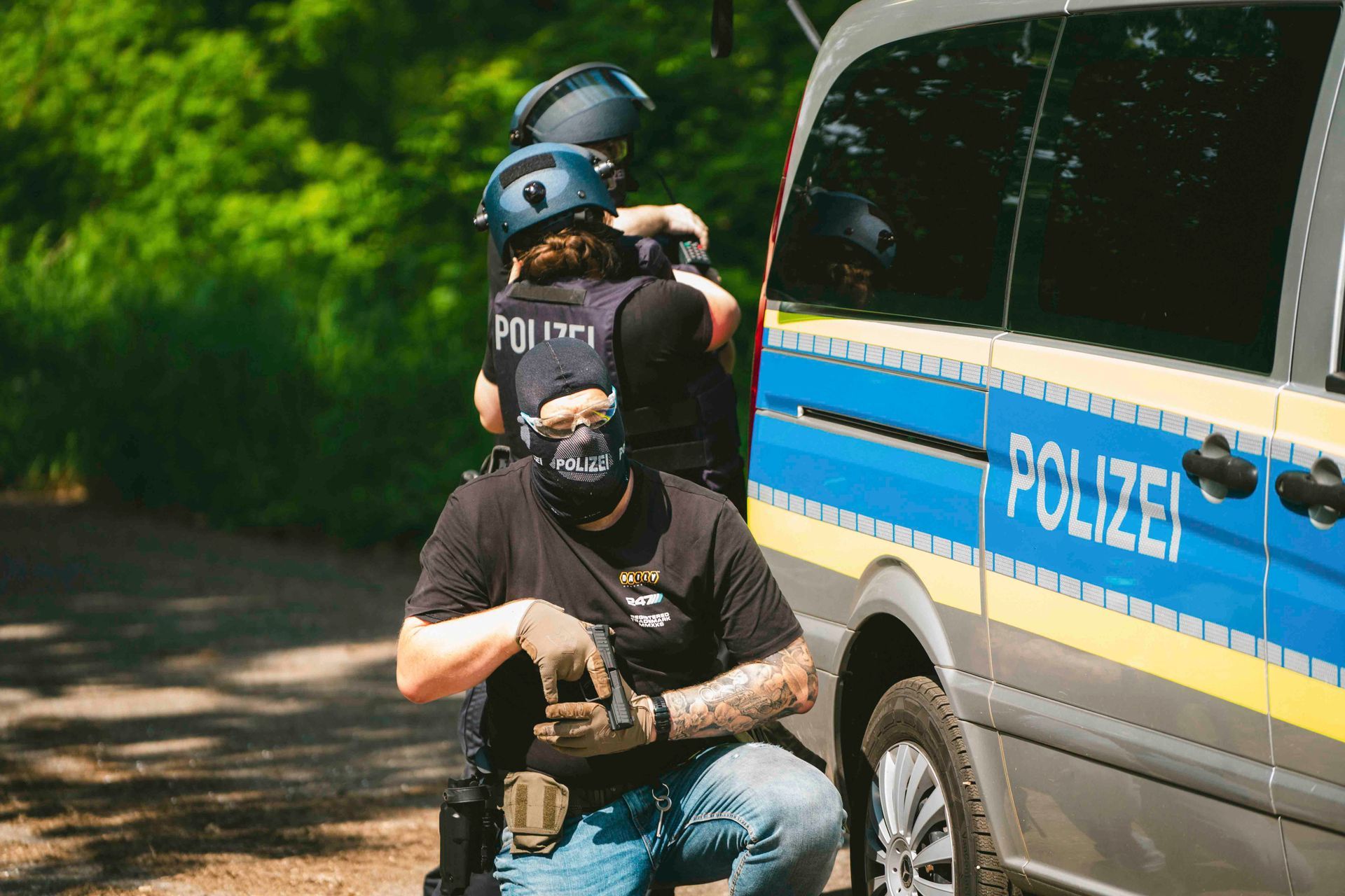 Polizisten in taktischer Ausrüstung in der Nähe eines Polizeiwagens, einer kniet und ist maskiert.