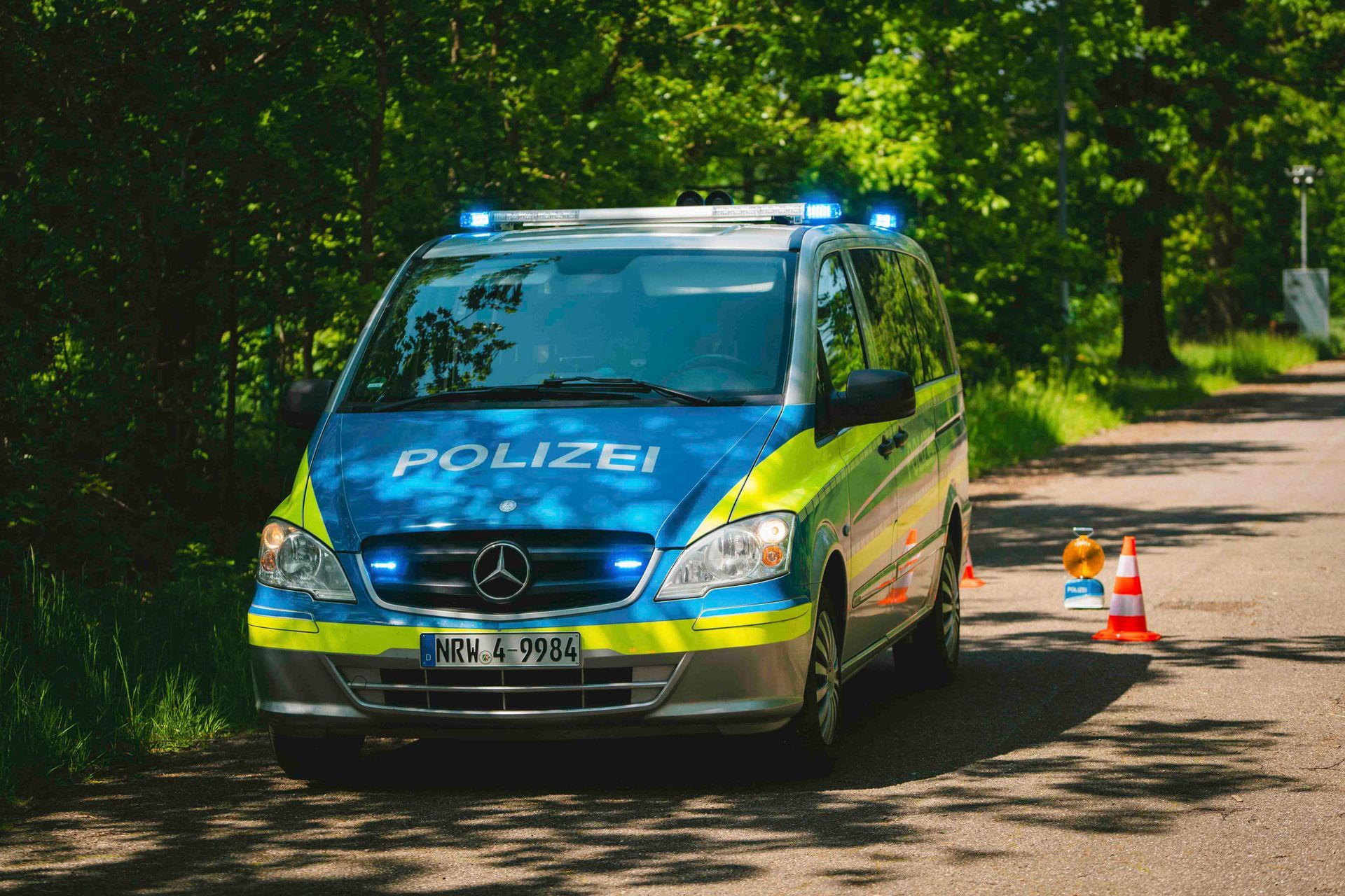 Ein deutscher Polizeiwagen parkt mit blinkenden blauen Lichtern und Verkehrskegeln auf einer Straße.