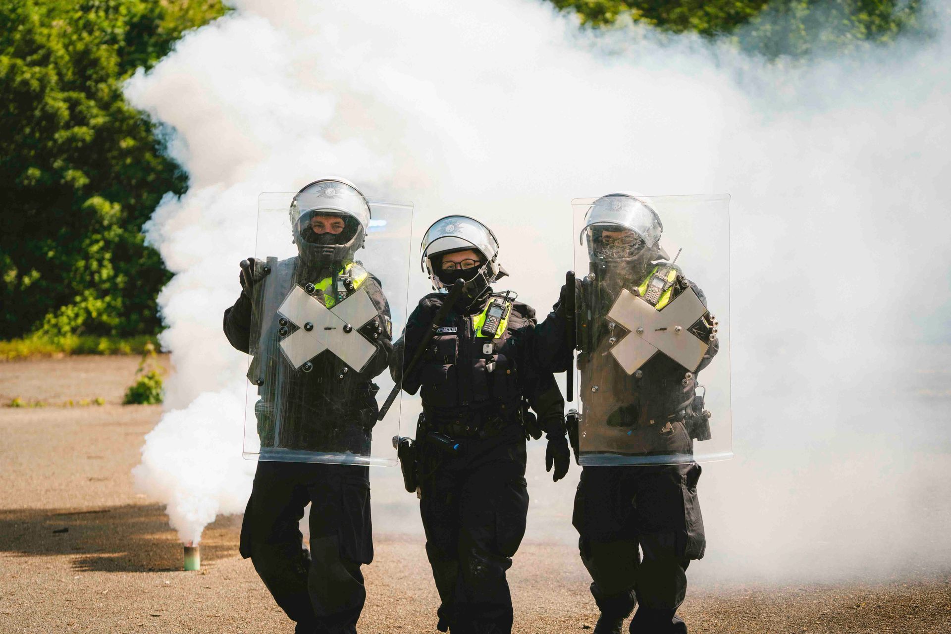 Drei Bereitschaftspolizisten in Gasmasken und Schutzausrüstung gehen durch eine Rauchwolke.