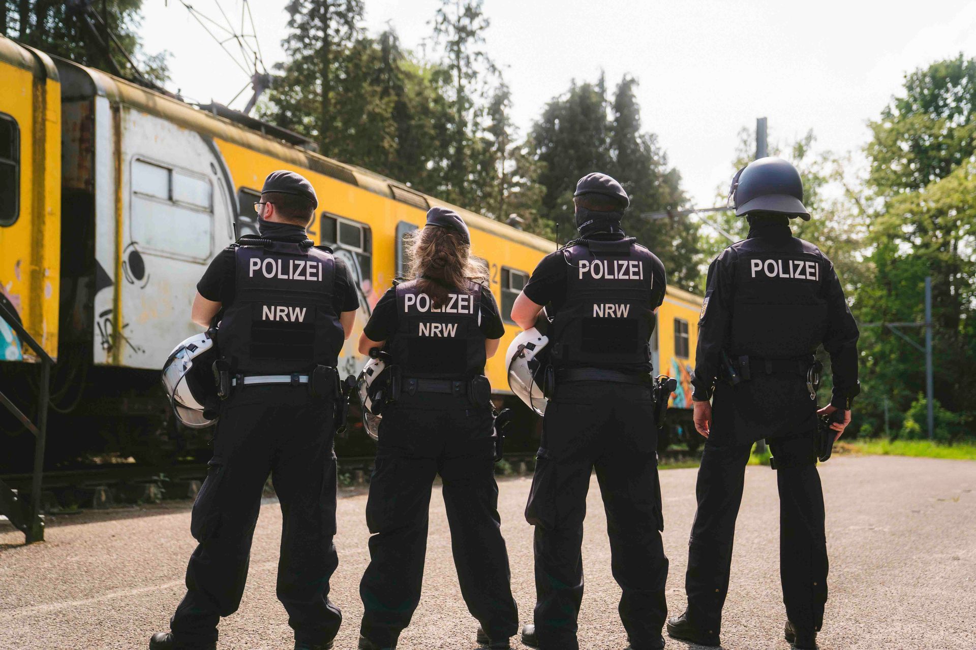 Vier uniformierte Polizisten stehen vor einem gelben Eisenbahnwaggon.