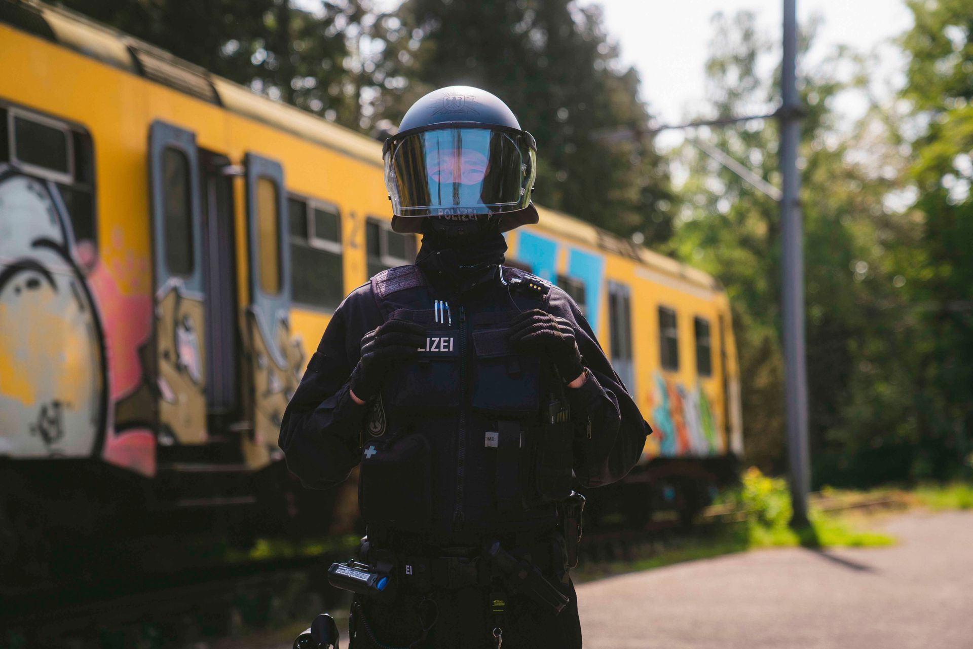 Eine Person in schwarzer Uniform und Helm steht vor einem gelben Zug mit Graffiti.