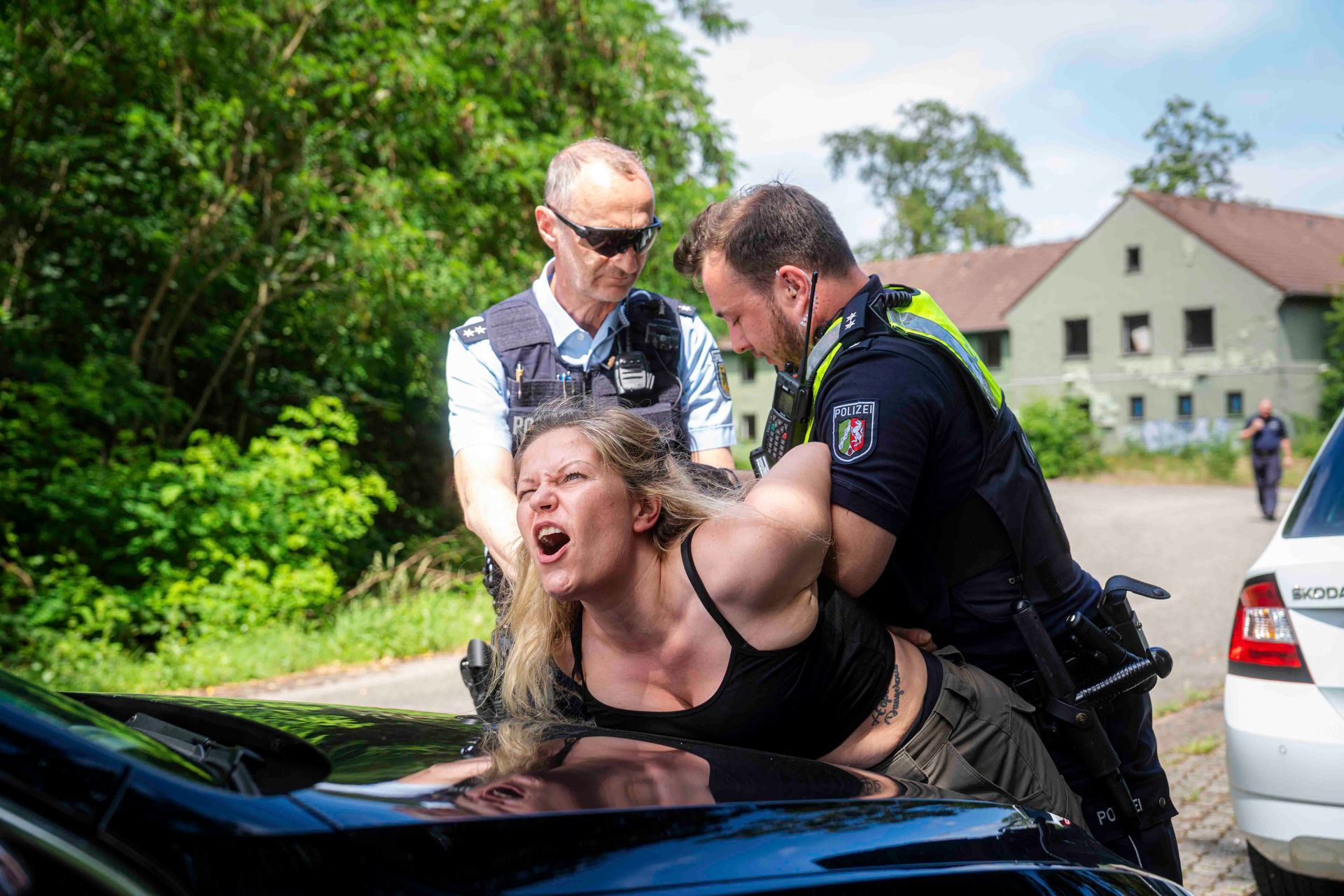 Zwei Polizisten nehmen eine Person fest, die sich an ein Auto lehnt und schreit.
