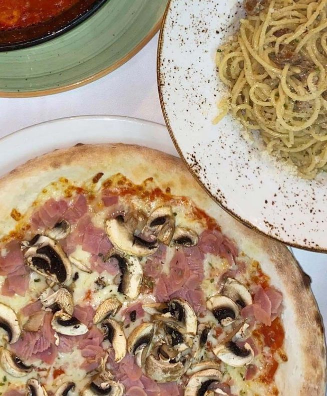 Una pizza y un plato de espaguetis están sobre una mesa.