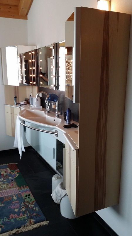 Waschbeckenbereich mit beleuchteten Spiegeln und Schrank aus Holz