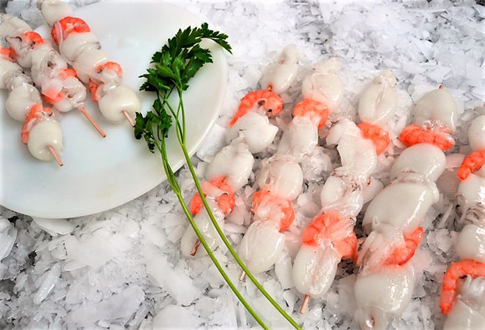 Un plato de brochetas de camarones en hielo al lado de un plato de brochetas de camarones en hielo.