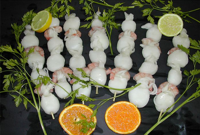 Un montón de calamares en brochetas con limones y naranjas sobre una mesa.