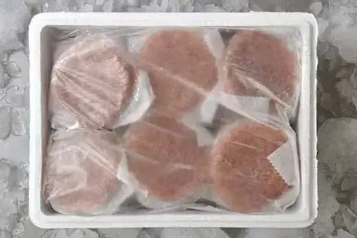 Una caja de hamburguesas congeladas envueltas en plástico sobre hielo.