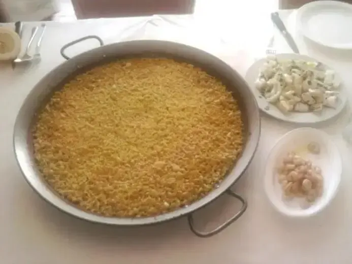 Una olla de arroz reposa sobre una mesa junto a platos de comida.