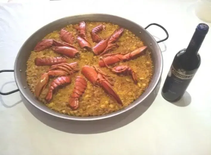 Una sartén llena de arroz y langostas junto a una botella de vino