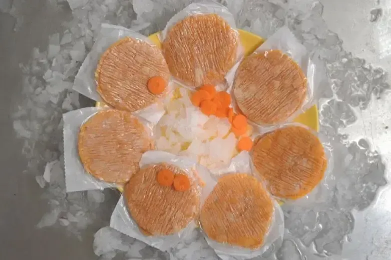 Un plato amarillo cubierto con hamburguesas y zanahorias sobre hielo.