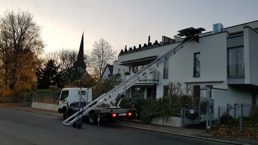 Vor einem Gebäude parkt ein Lastwagen mit einer daran befestigten Leiter.