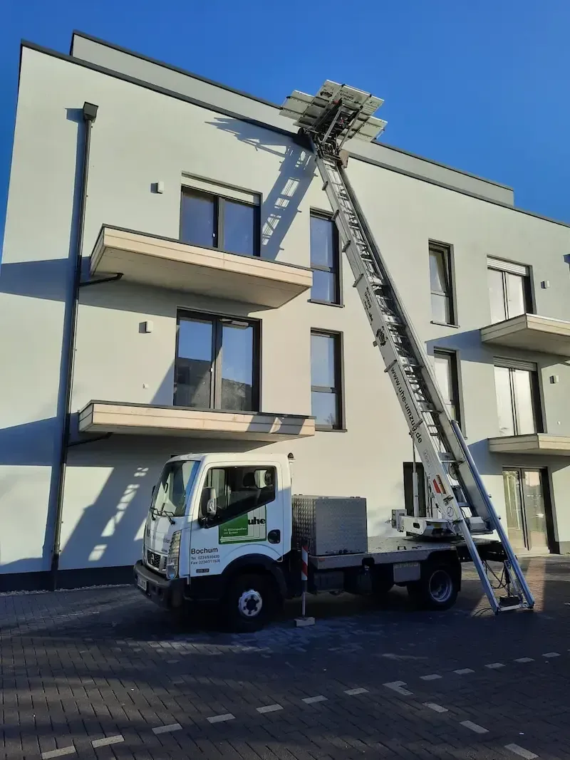 Ein weißer LKW mit einer daran befestigten Leiter steht vor einem Gebäude