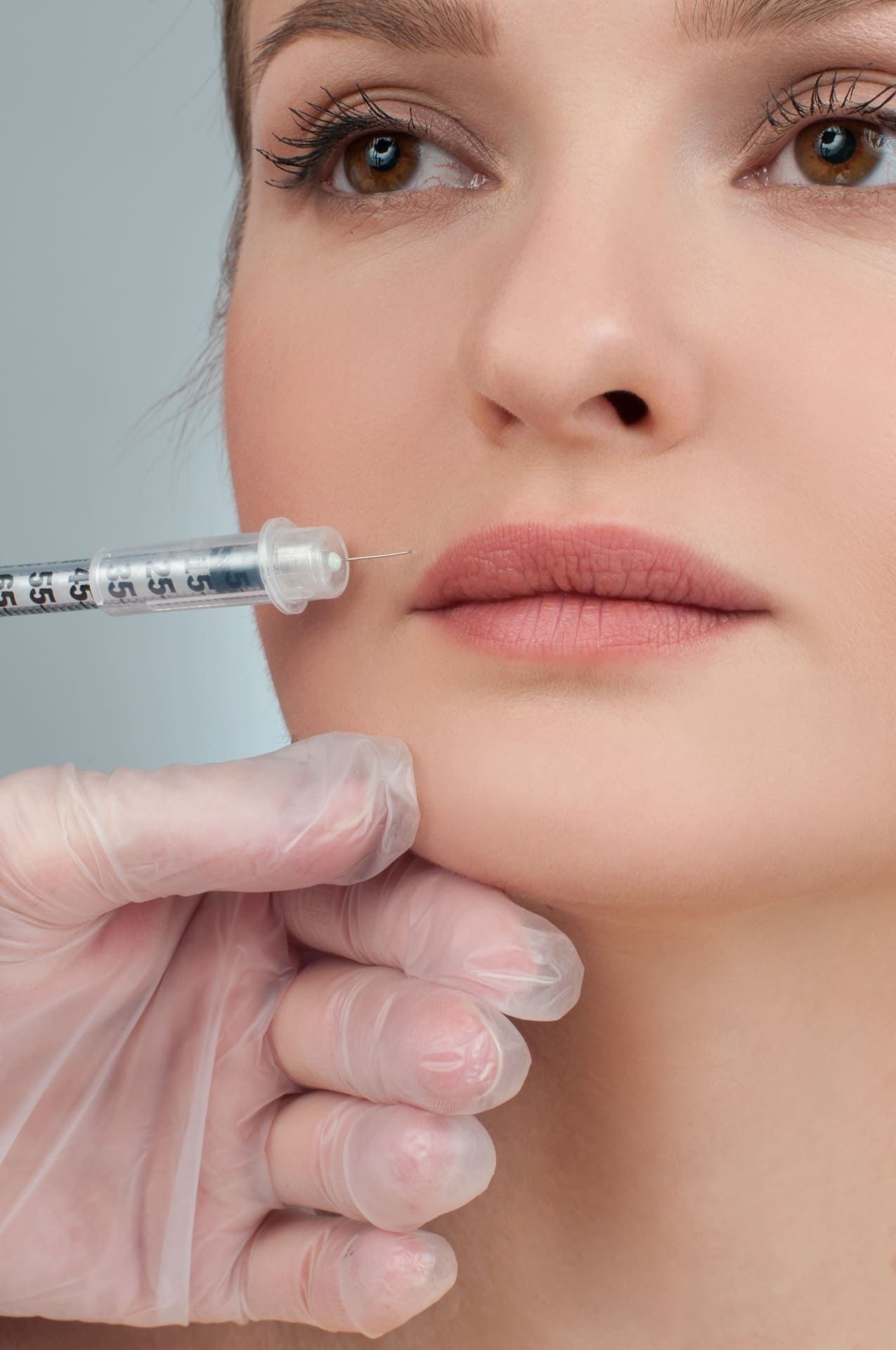 Mano enguantada sosteniendo una jeringa cerca de los labios de una mujer durante un procedimiento de inyección cosmética.