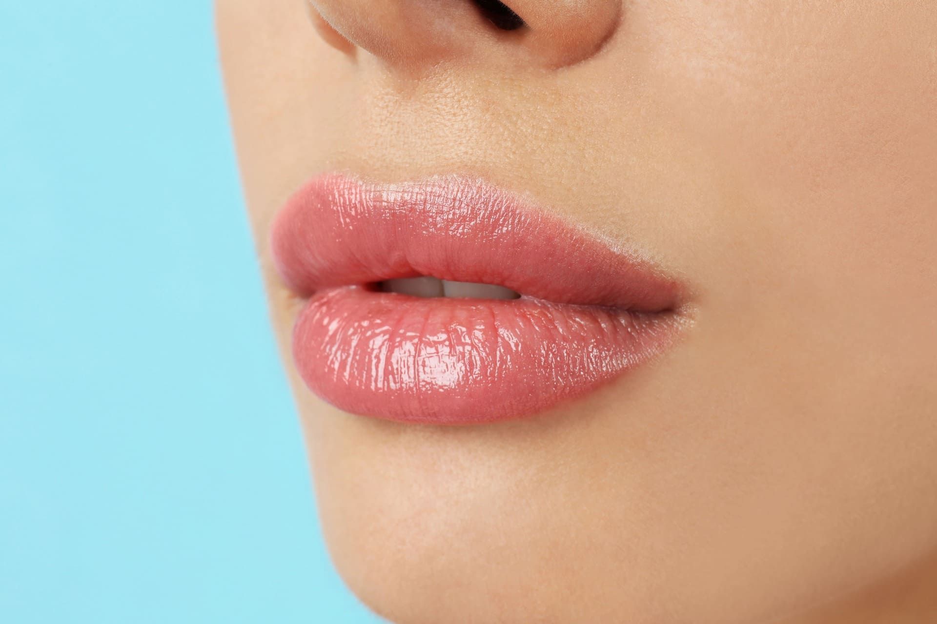 Primer plano de unos labios rosados brillantes sobre un rostro con fondo azul claro.