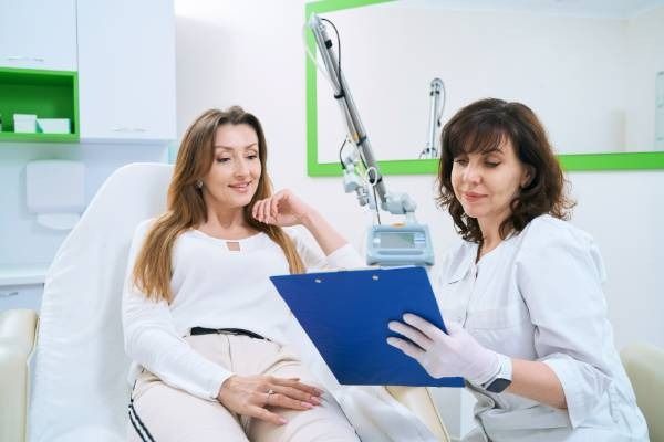 Paciente y médico revisando un portapapeles azul en un consultorio médico bien iluminado.