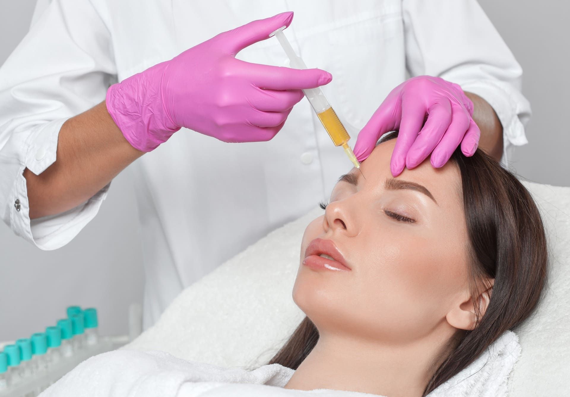 Un profesional sanitario con guantes aplica suero en la frente de una mujer durante un tratamiento facial.