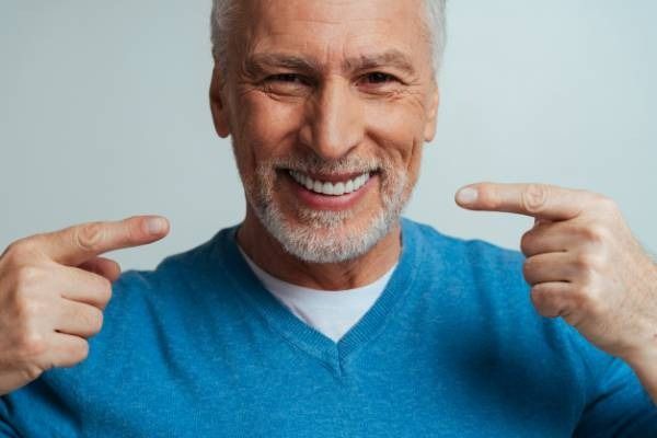 Un hombre sonriente con un suéter azul se señala la cara con ambas manos.