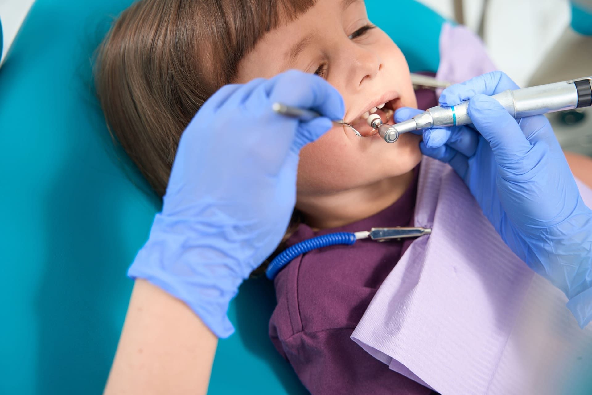 Dentista limpiando los dientes de un niño con guantes azules y herramientas dentales.
