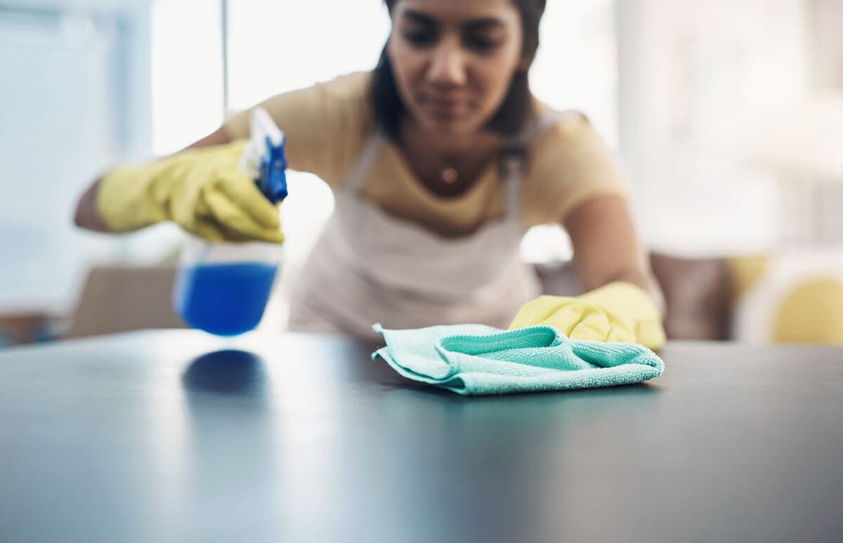 Una mujer está limpiando una mesa con un paño y una botella de spray.