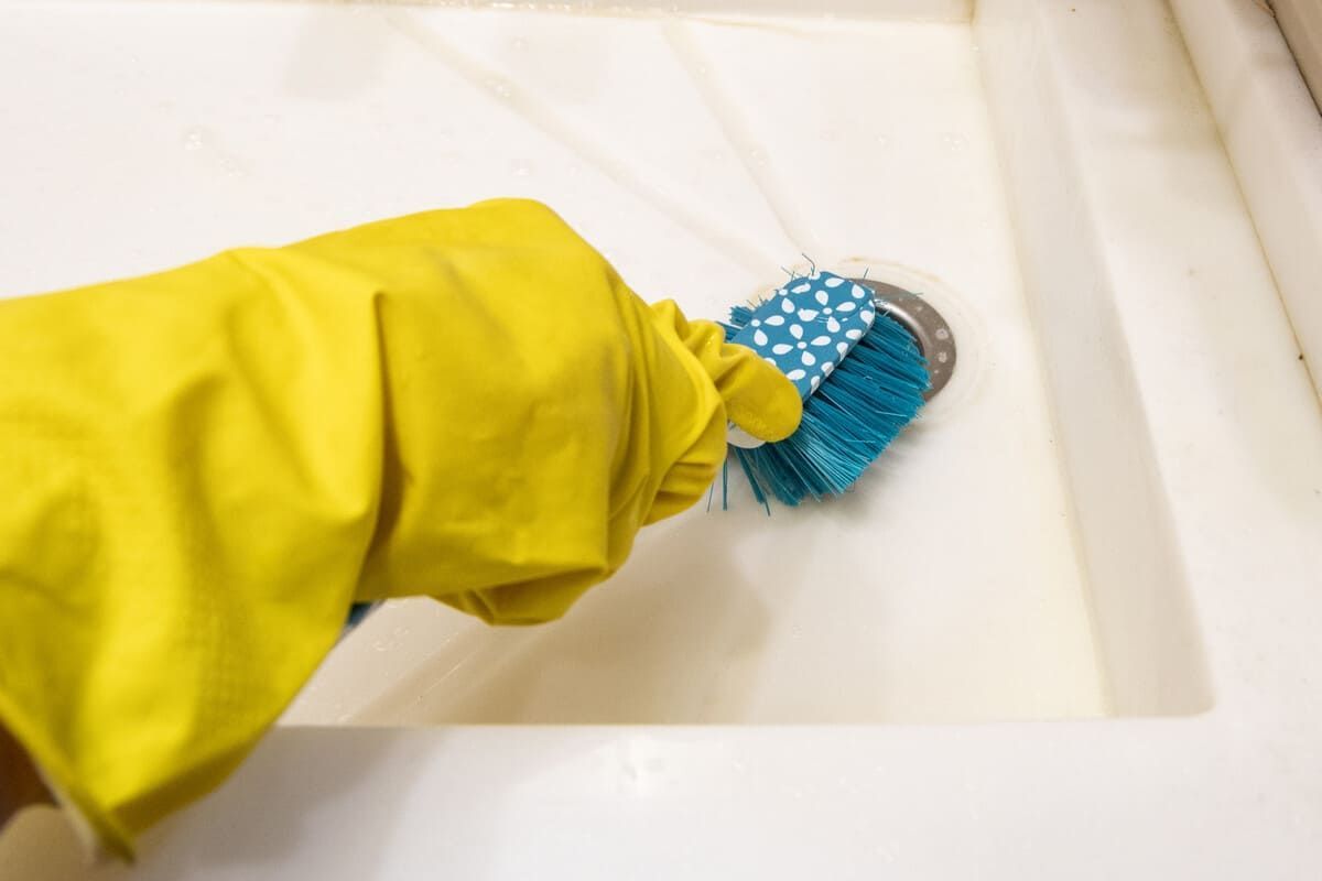 Una persona que lleva un guante de goma amarillo está limpiando un fregadero con un cepillo.