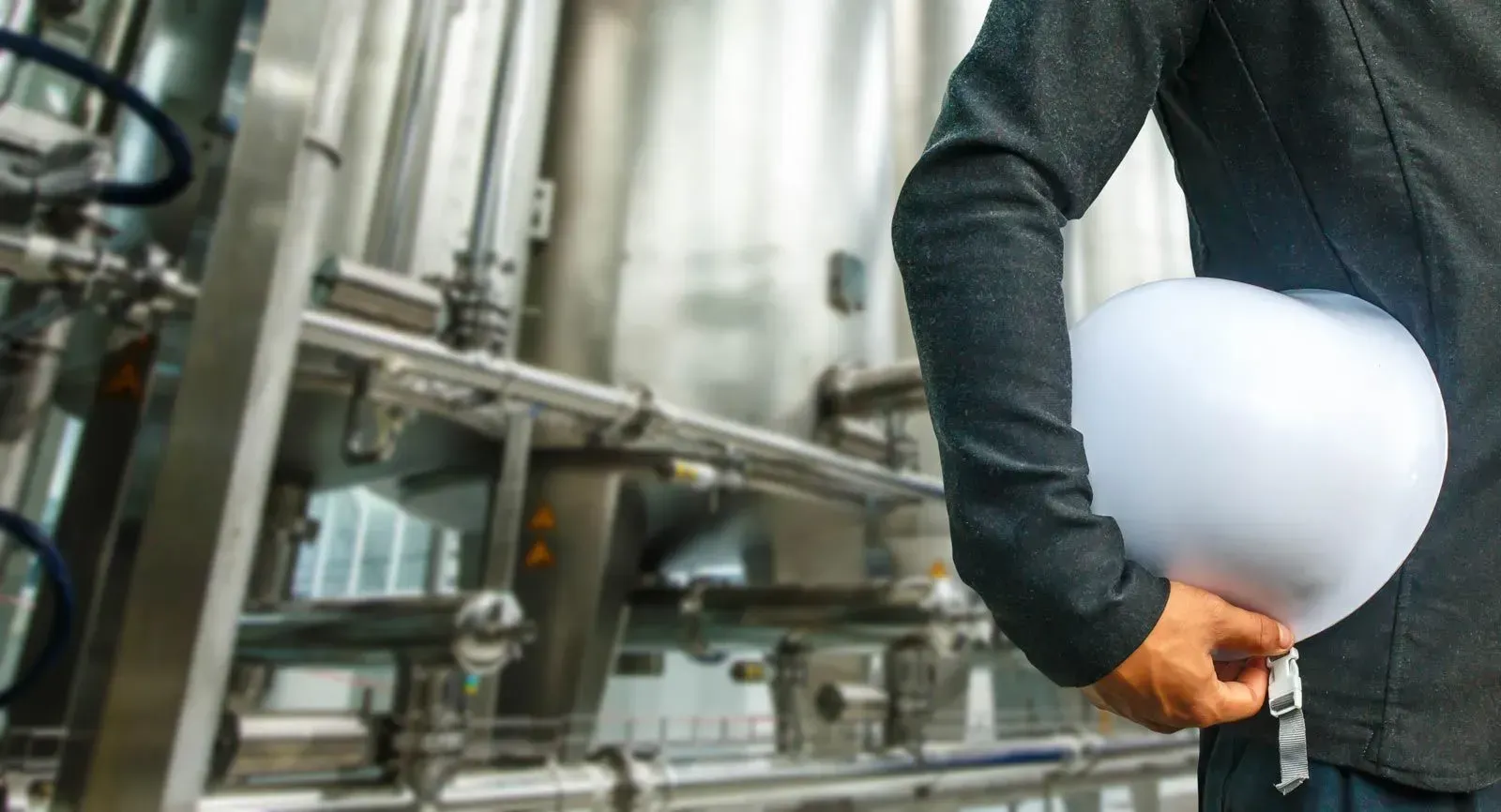 Ein Mann mit einem Schutzhelm steht vor einer Fabrik.