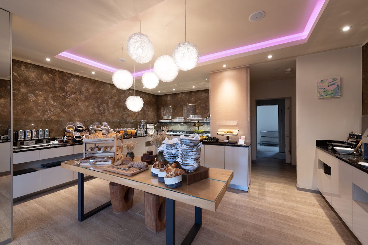 Heller, moderner Buffetraum mit Tischen, Speisenauslagen und rosa Akzentbeleuchtung zum Frühstück Alzey.