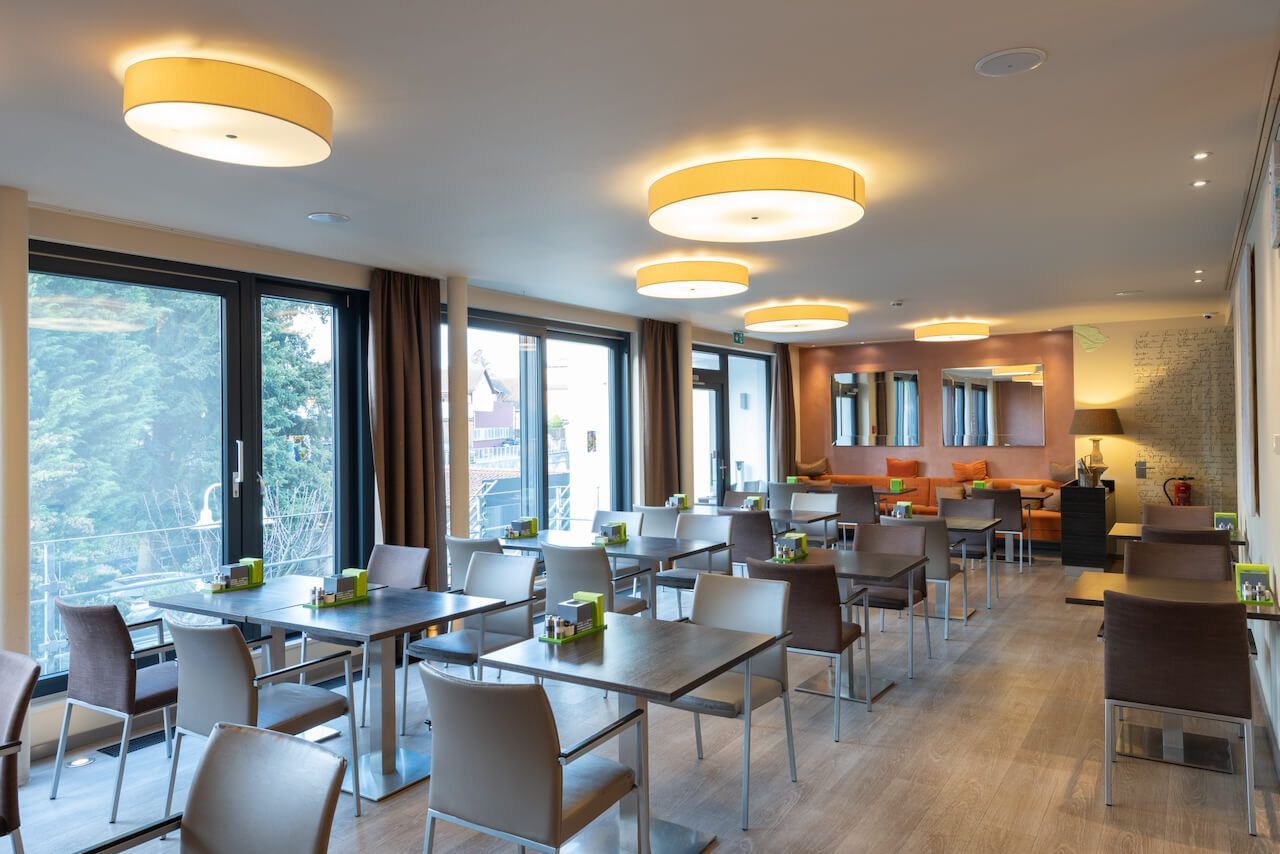 Moderner Frühstücksraum mit Tischen, Stühlen, großen Fenstern und warmem Deckenlicht in Kibo.