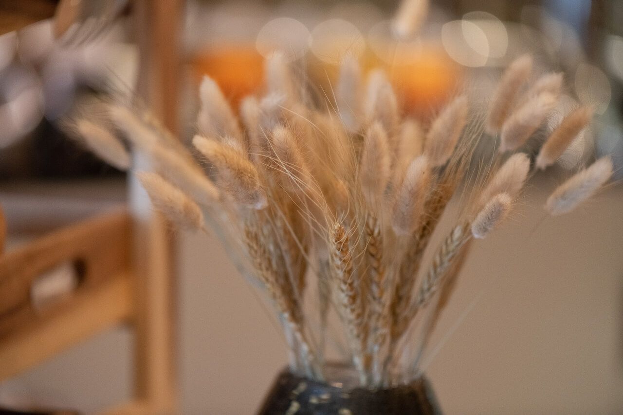 Getrocknete Weizenähren in einer Vase auf einem Tisch, im Hintergrund warmes, verschwommenes Café-Licht.
