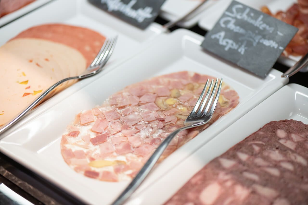 Aufgeschnittene Wurstwaren, angerichtet auf Tabletts mit Serviergabeln an einer Feinkosttheke zum Frühstück-Donnersberg.