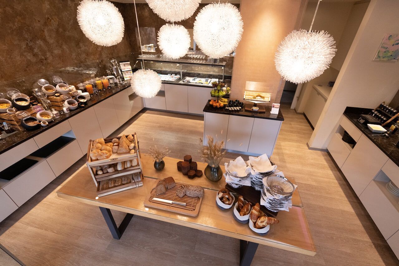Buffet mit Gebäck und Snacks in einem hellen Speisesaal mit hängenden Kugellampen im ART-Hotel Braun.