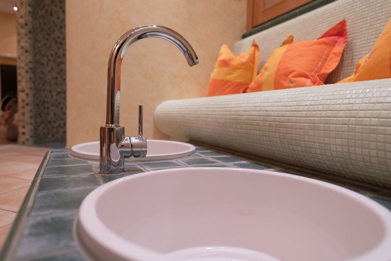Sitzbank im SPA mit verchromter Armatur neben einem beigen Sofa und orangefarbenen Kissen in Kirchheimbolanden.