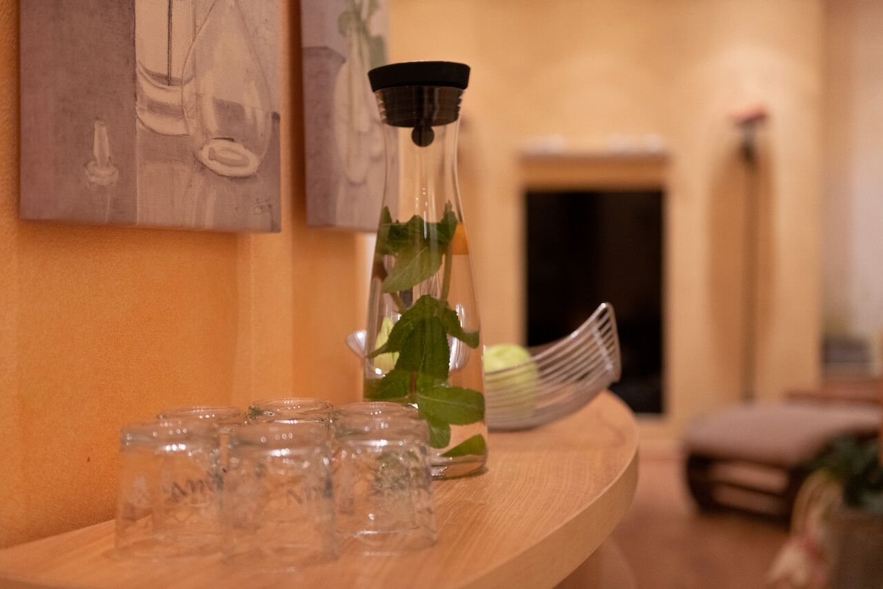 Ein Glasgefäß mit Wasser und grünen Blättern auf einem Holzregal in einem sanft beleuchteten Flur der Wellness-Oase bei Rheinhessen.