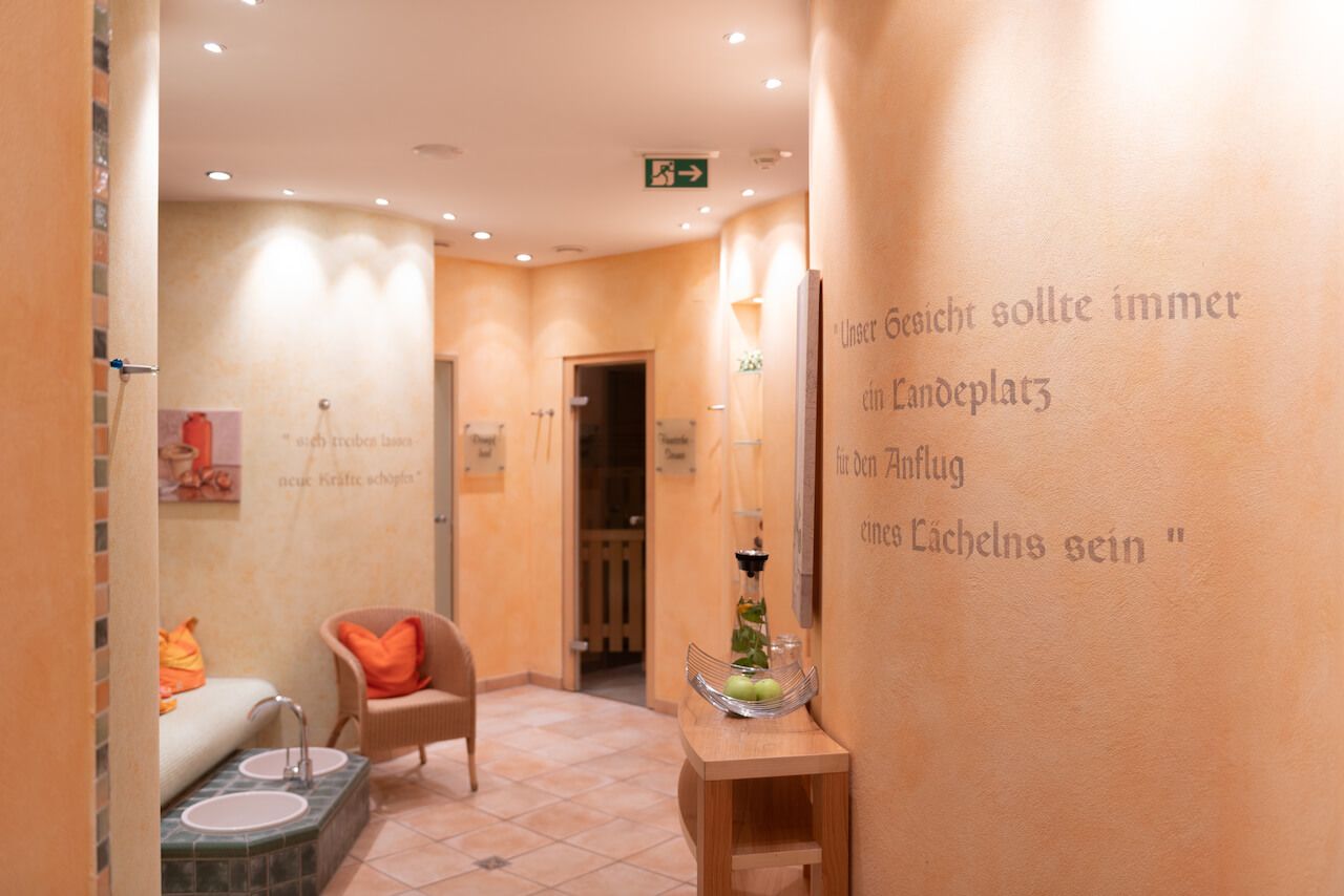 Gemütlicher Flur mit beigen Wänden, Einbaustrahlern, Stühlen, einer Tür und französischem Text an der rechten Wand. Pfalzsauna.