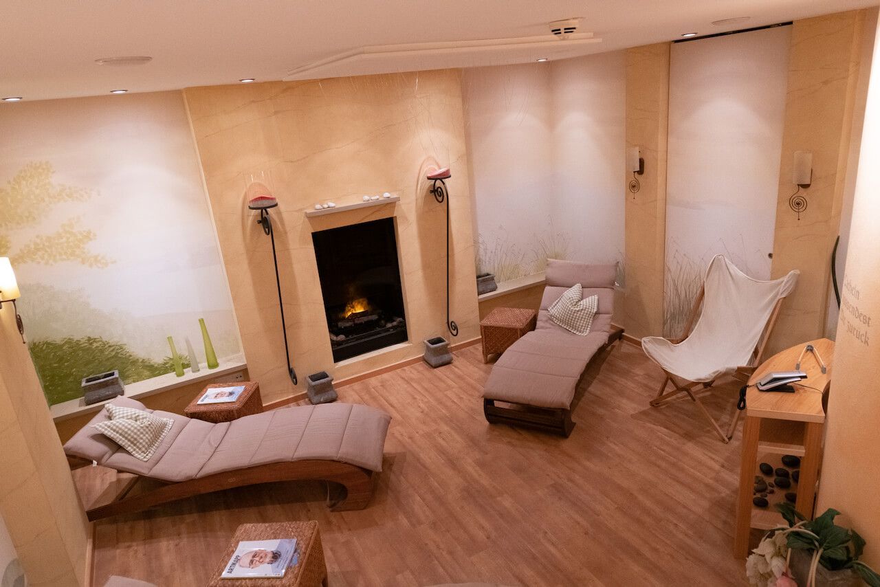 Entspannungsraum mit Chaiselongues, Korbsesseln und Kamin in warmem Holzinterieur in der Sauna Kirchheimbolanden.