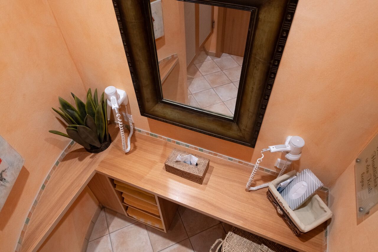 Kleiner Badezimmerwaschtisch mit Holzplatte, Spiegel, Waschbecken, Pflanze und Toilettenartikeln an orangefarbenen Wänden im SPA.
