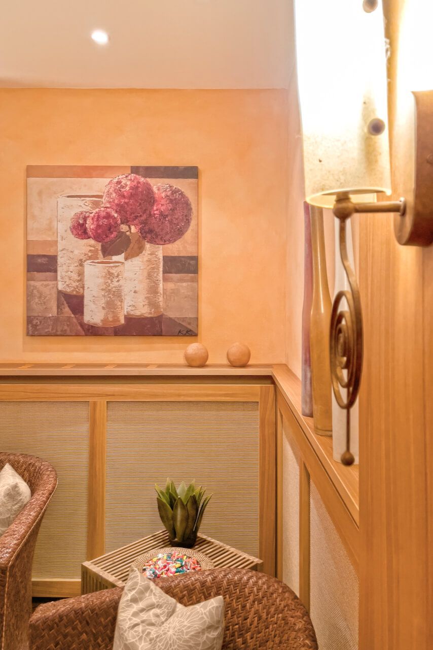 Warme beige Ecke mit floraler Wandkunst, Korbstühlen und einer Wandleuchte in einem gemütlichen Zimmer in der Wellness-Oase