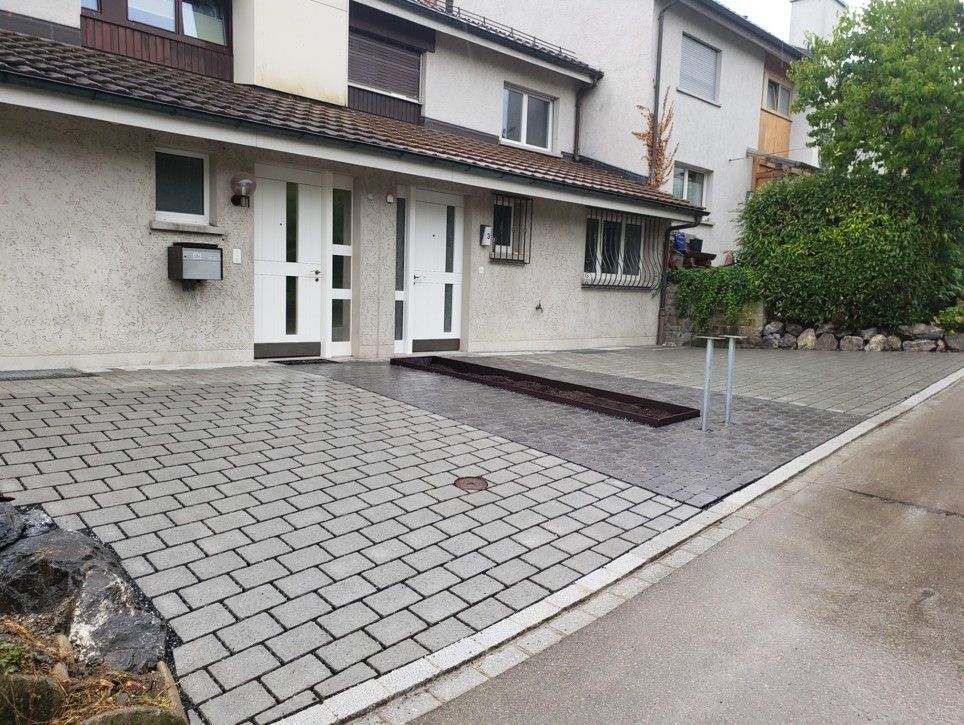 Eine Person mit grünen Handschuhen stutzt einen Busch mit einer Gartenschere.