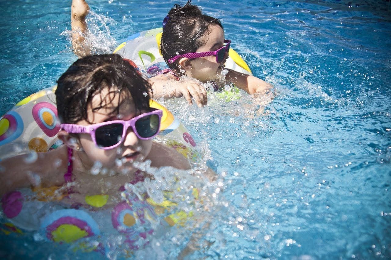 Zwei junge Mädchen mit Sonnenbrillen schwimmen in einem Pool.