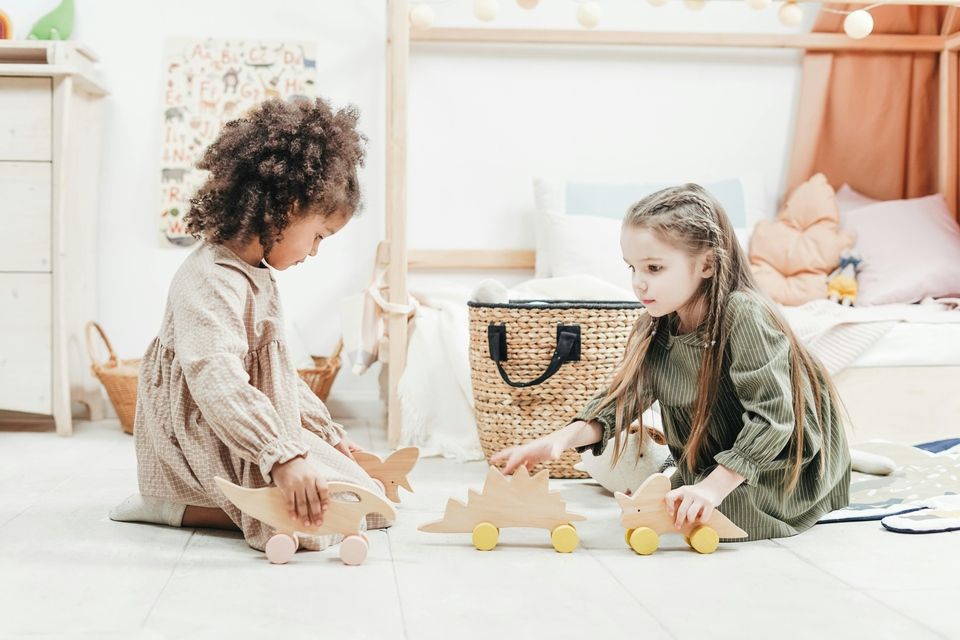 Zwei kleine Mädchen spielen in einem Zimmer mit Holzspielzeug.