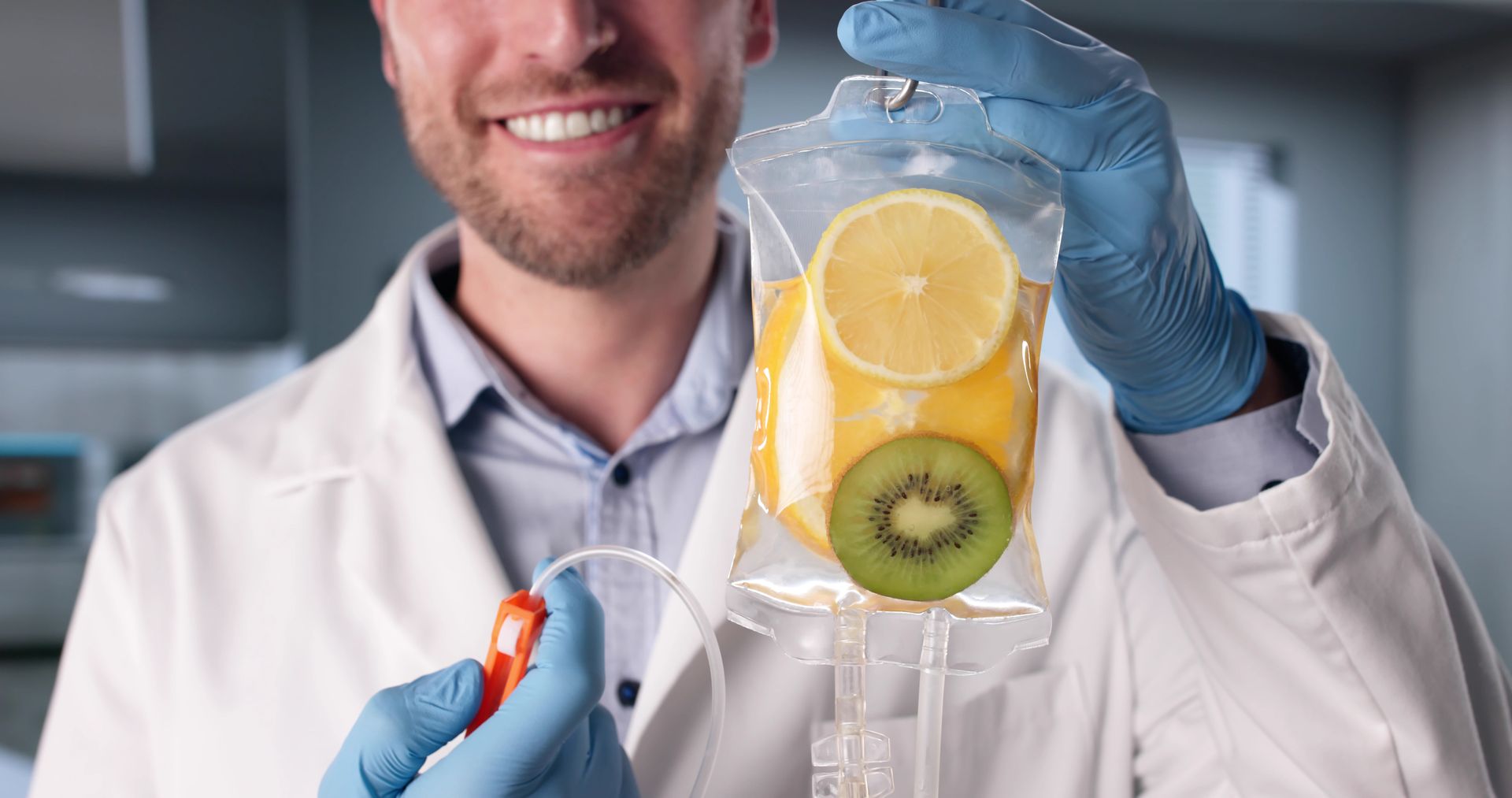 Eine lächelnde Person in Laborkittel und Handschuhen hält einen mit Früchten gefüllten Infusionsbeutel.