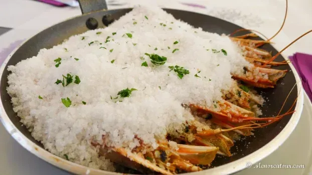 Una sartén de camarones cocidos cubiertos con una gruesa capa de sal blanca, espolvoreados con hierbas verdes.