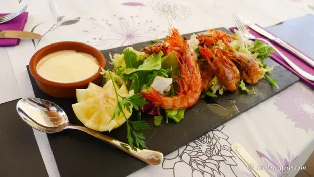 Camarones a la plancha y ensalada sobre pizarra negra, con salsa y limón. Servidos en una mesa con mantel floral.