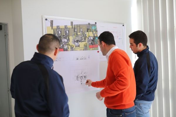 Tres hombres miran un diagrama en una pizarra blanca.