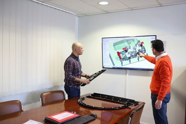 Dos hombres miran un dibujo en una pantalla en una sala de conferencias.