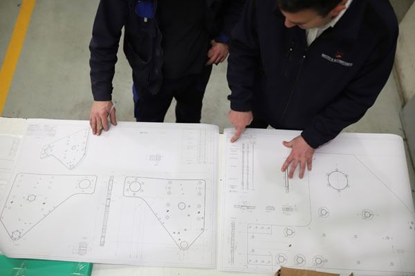 Dos hombres miran dibujos en una mesa.