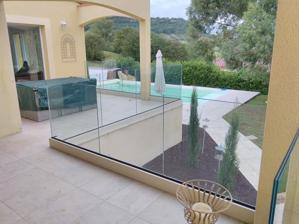 Terrasse donnant sur une piscine et un jardin, avec balustrade en verre et sol carrelé beige
