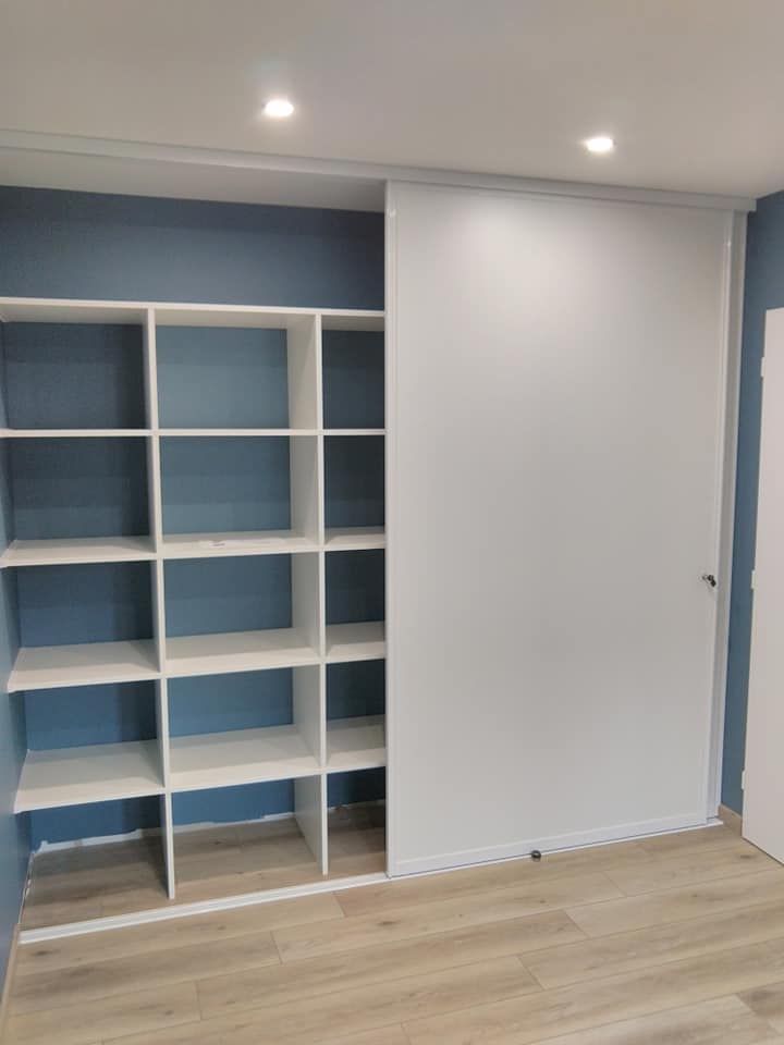 Étagères bleues encastrées à côté d'une porte de placard coulissante blanche dans une petite pièce au parquet clair