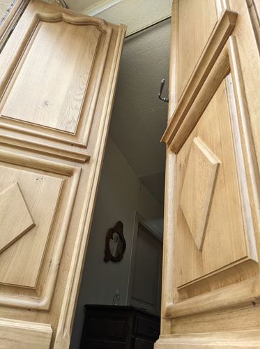 Des portes doubles en bois s'ouvrent sur un couloir sombre avec une petite horloge murale.
